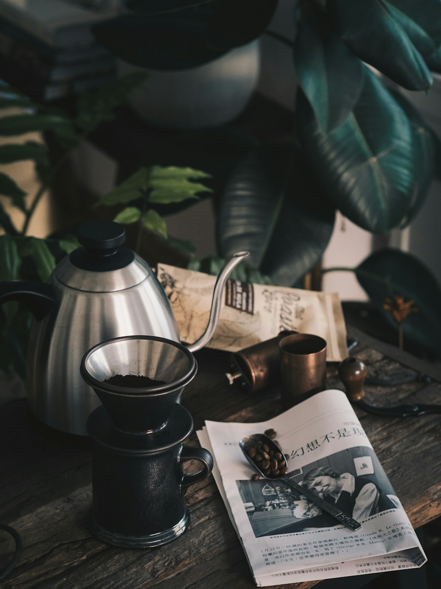A coffee grinder, teapot, newspaper, and plant in morning light